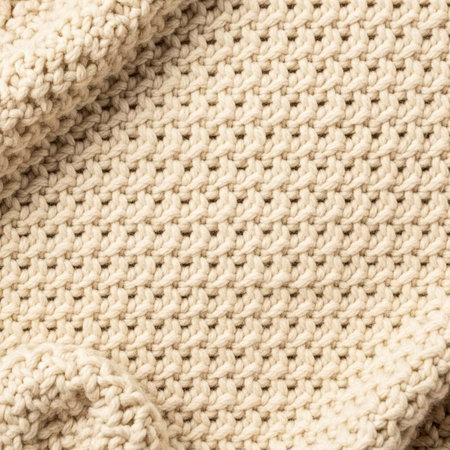 A close-up view of a cream-colored knitted fabric with a textured weave pattern