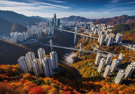 Aerial view of a modern cityscape with a large bridge and skyscrapers surrounded by autumn foliage...