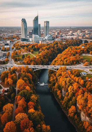 Aerial view of a city with a river and bridge surrounded by vibrant autumn trees and modern skyscrapersの写真素材