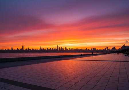 A vibrant city skyline at sunset with a colorful sky reflected on a tiled waterfront promenadeの写真素材