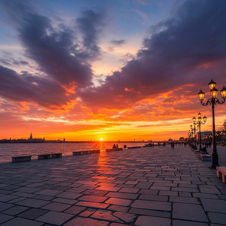 A serene waterfront promenade at sunset with a vibrant sky and city skyline in the distance.の写真素材