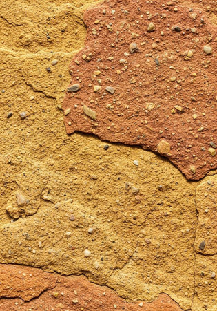 A close-up view of a textured, cracked, and weathered surface with orange and yellow hues