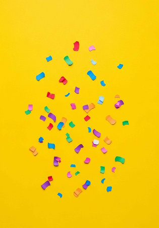 Multicolored confetti on yellow background, festive and celebratory atmosphere, party decoration