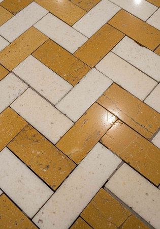 A close-up view of a herringbone patterned floor made of shiny rectangular tiles in white and brown colors