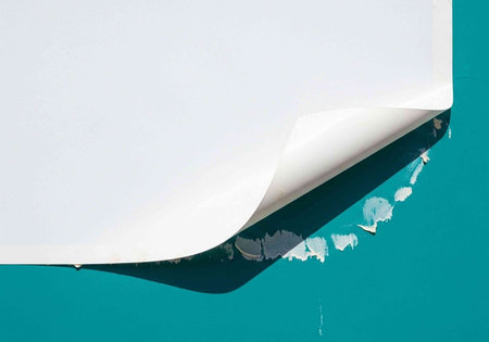 A close-up view of a peeled back paper revealing a teal background with torn edges and a white surface