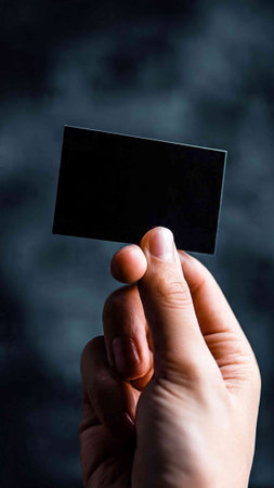 Hand holding a black business card on a dark background with copy space