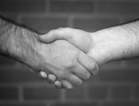 A black and white handshake in front of a brick wall backdrop.の写真素材