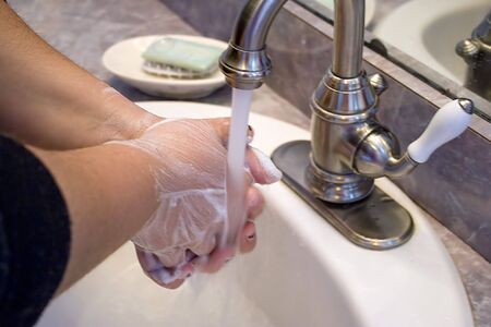 A person washing and rinsing off their hands in the bathroom sink.