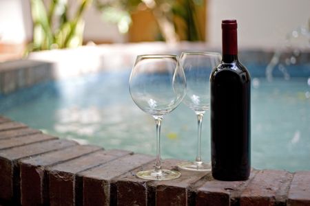 A red wine bottle and two empty glasses by the pool.  の写真素材