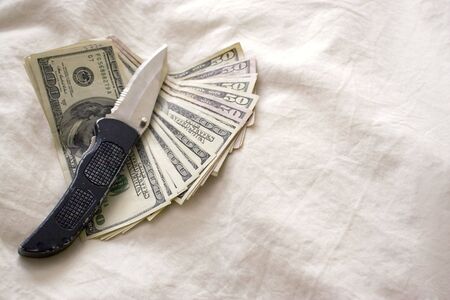 A knife and some fanned out cash laying on a bed.の写真素材