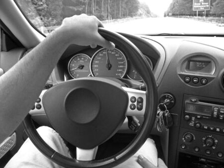 A man holds the steering wheel with one hand while driving on the highway.の写真素材