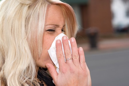 This young woman sneezing into a tissue either has a cold or really bad allergies.の写真素材