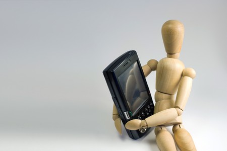 Wooden dummy grasping a mobile smartphone in his arms.の写真素材