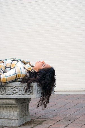 A closeup of a pretty Indian woman laying on a bench outdoors.の写真素材