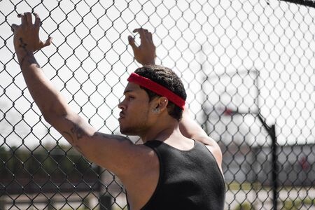 A young basketball leaning up against the chain linked fence at the basketball court.