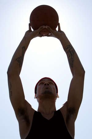 A silhouette of a young basketball player holding the ball up to the sky.の写真素材