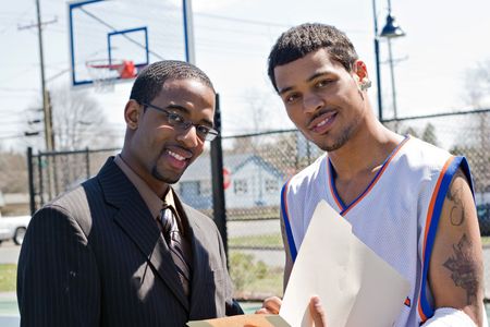 A basketball coach in a business suit sharing a play with a player on the team.   He could be also be recruiter trying to get him to sign a contract.の写真素材