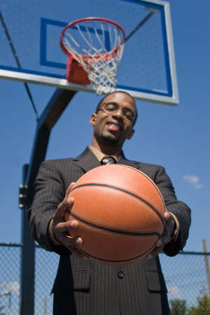 A young man in a business suit posing with a basketball.  He could be a coach player recruiter scout or trainer. Shallow depth of field with focus on the ball.の写真素材
