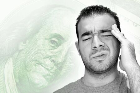 A young man holds his head in anguish as he thinks about his money problems with either debt or unemployment.の写真素材