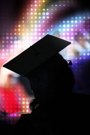 A recent university or high school graduate posing in her cap and gown in front of a rainbow halftone background.の写真素材