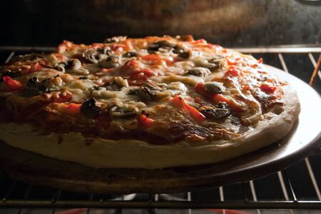 A fresh homemade mushroom and pepper pizza fresh out of the oven and ready to slice. Shallow depth of field.の写真素材