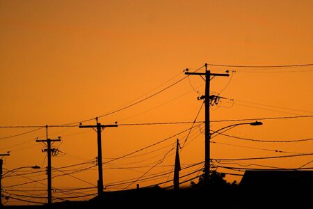 Silhouettes of the power lines and wires in a residential neighborhood backlit by the evening sky.