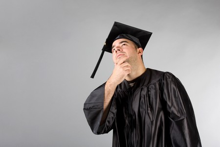 A recent college or high school graduate in his cap and gown thinking and looking contemplative.の写真素材