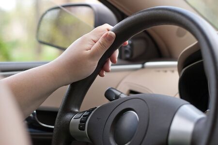 A woman holding the steering wheel of a car with one hand while driving.