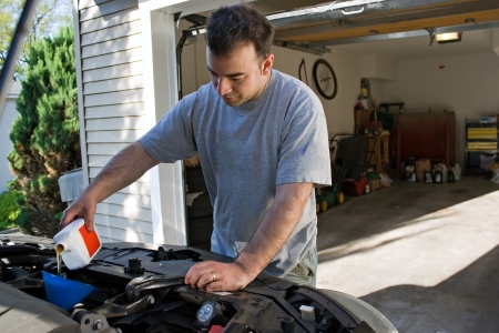 A young man adding oil to his cars engine at the end of an oil change.の写真素材
