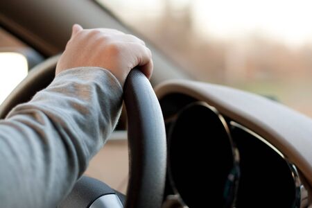 A woman holding the steering wheel of a car with one hand while driving.の写真素材