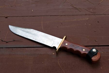 A large bowie knife laying on the wooden table used for hunting or camping.の写真素材
