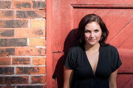 A pretty young woman in a black dress leaning against an old doorway. の写真素材