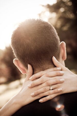 A woman hugs her fiance by placing her hands around his neck in sepia tone. Shallow depth of field with focus on the ring.の写真素材