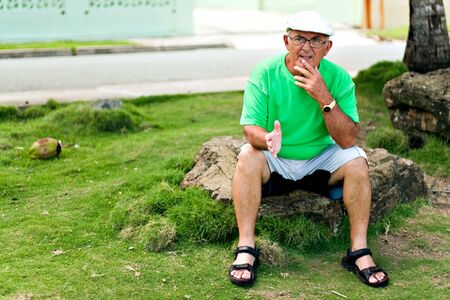 A older Hispanic senior citizen man sits outdoors in a tropical setting. の写真素材