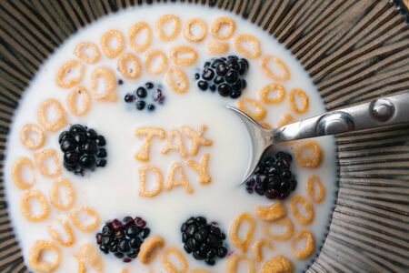 The words TAX DAY spelled out of letter shaped cereal pieces floating in a milk filled cereal bowl.