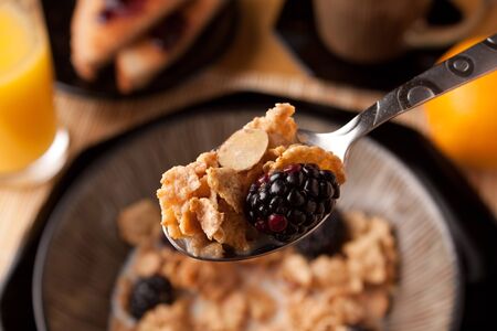 Close up of a spoon full of breakfast cereal flakes with almonds and blackberries.  Shallow depth of...