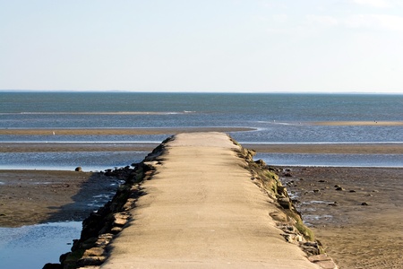 A jetty at the beach extends out into the ocean around low tide.