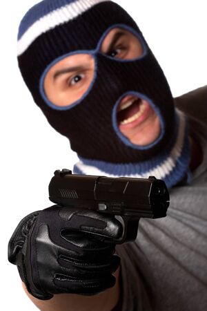 An angry looking man wearing a ski mask pointing a black handgun at the viewer. Shallow depth of field with sharpest focus on the gun.の写真素材