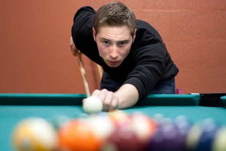 A young man lines up his shot as he breaks the balls for the start of a game of billiards. Shallow depth of field.の写真素材