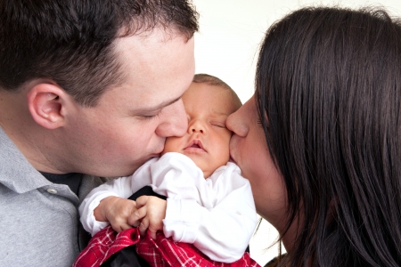 A newborn baby is held by her mother and father as they kiss her cheeks.の写真素材