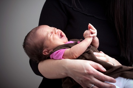 A mom holds a young newborn baby girl in her arms that is upset and crying.の写真素材