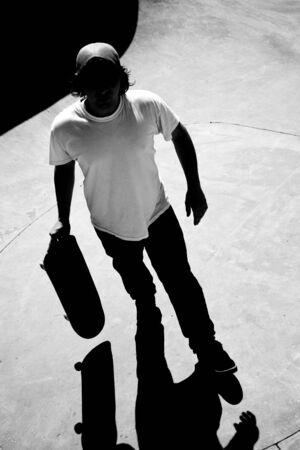 Silhouette of a skateboarder standing inside the pool at the skate park with strong contrast and dramatic shadows. Black and white.の写真素材