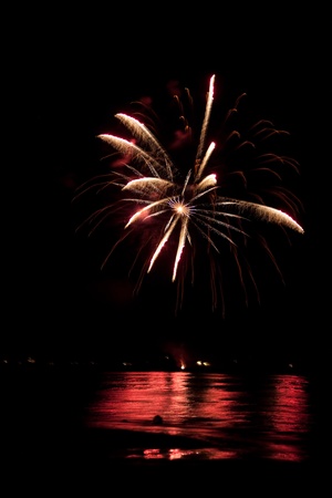 Beautiful fireworks going off over the dark night sky reflecting over the water.