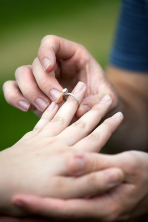 Man placing a diamond engagement ring on the finger of his fiance.  Shallow depth of field with focus on the ring.の写真素材