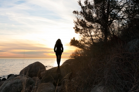 Silhouette of a woman standing in front of the sunset at the New England shoreline.の写真素材