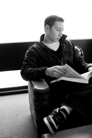 A young college aged man reading a book at the library in black and white.の写真素材