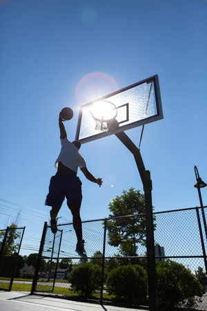 A young basketball player going up for a dunk.  Intentionally back lit with bright lens flare coming...