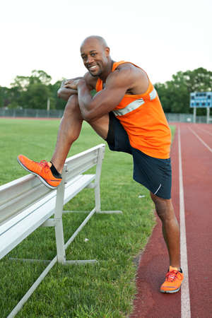 African American man in his 30s stretching out before a run at a sports track outdoors.