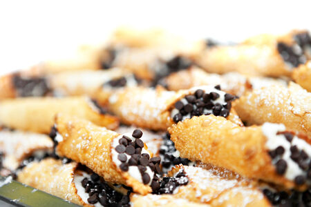 Tray full of freshly filled cannolis with chocolate chips and confectioners sugar. Shallow depth of...