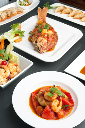 Variety of Thai style whole fish red snapper sweet and sour shrimp gyoza dumplings sesame breads seafood salad and other spicy Thai dishes.の写真素材